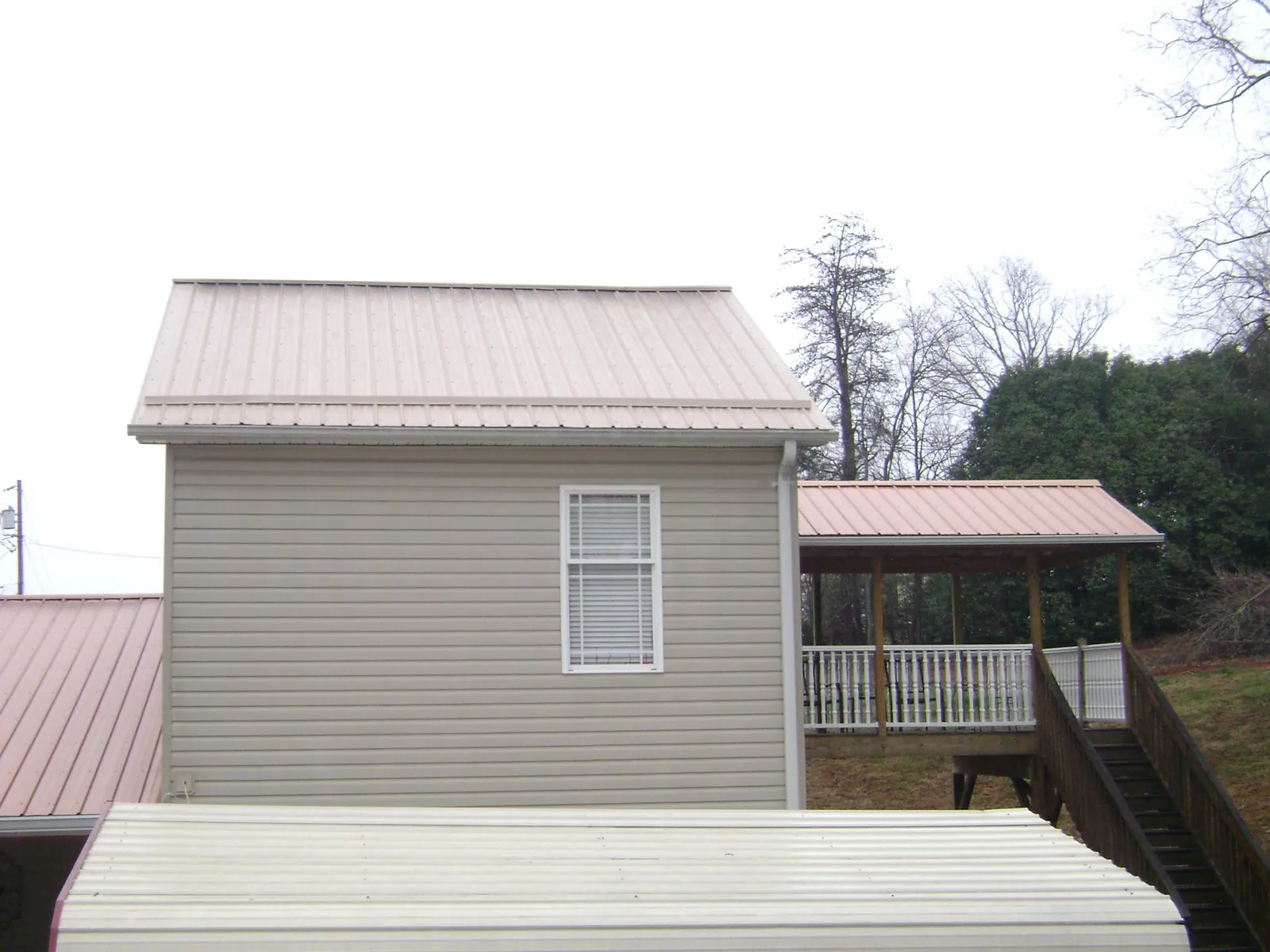 Tan metal roofs on a two story addition and attached porch, from a Roof Replacement job in Bristol